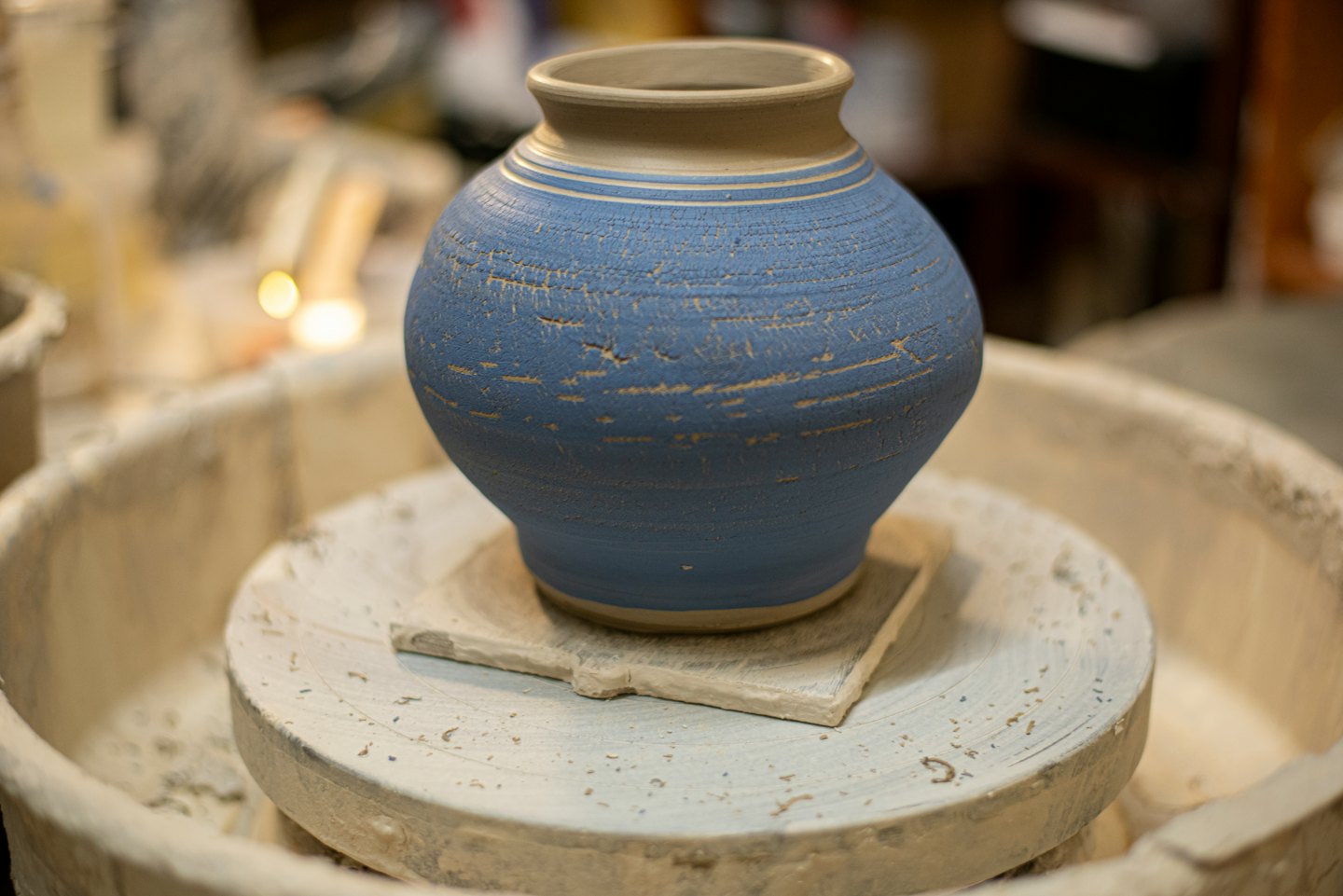Un jarrón de cerámica hecho a mano, azul y beige, descansa sobre un torno de alfarero.