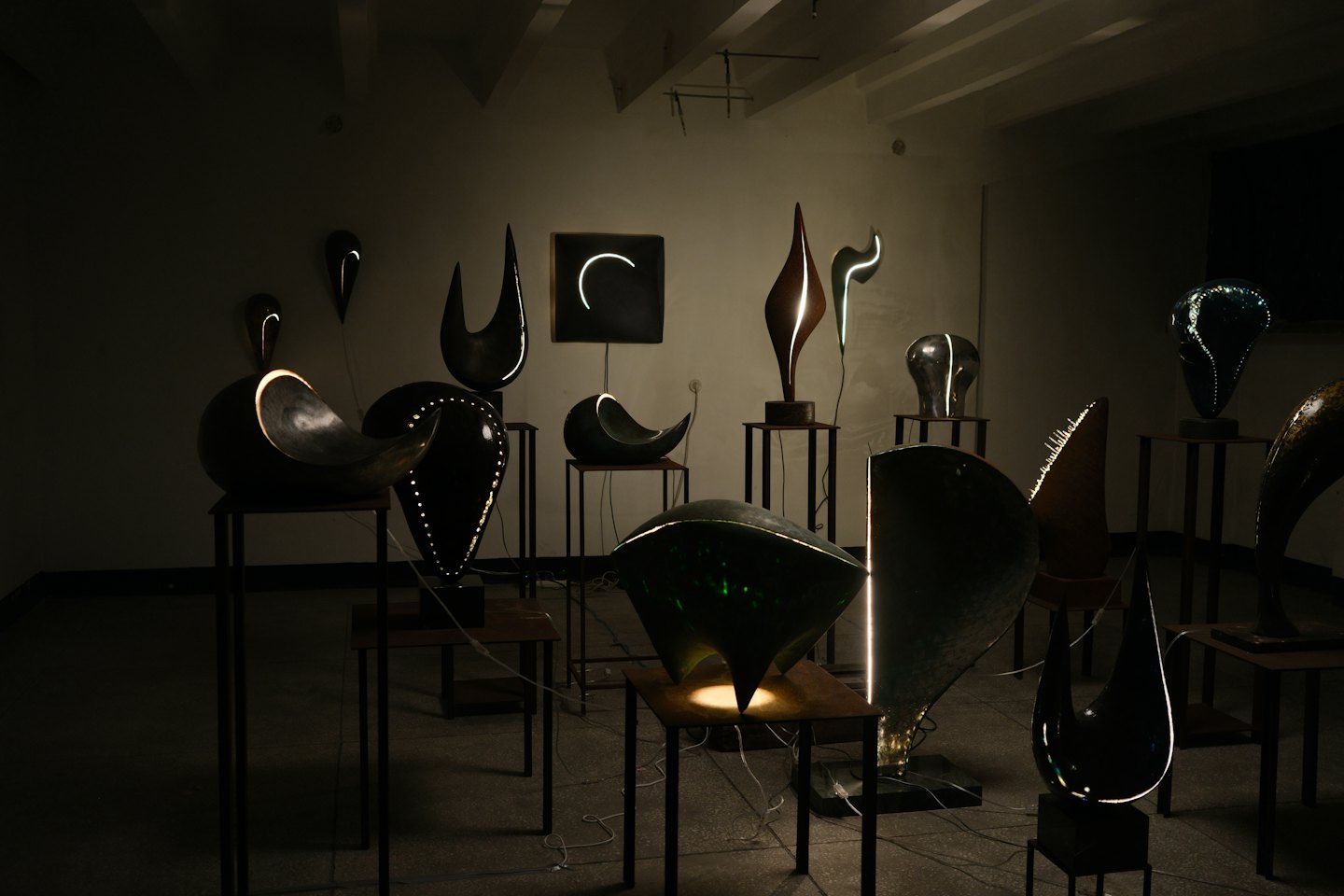 Esculturas abstractas iluminadas en pedestales en una galería.