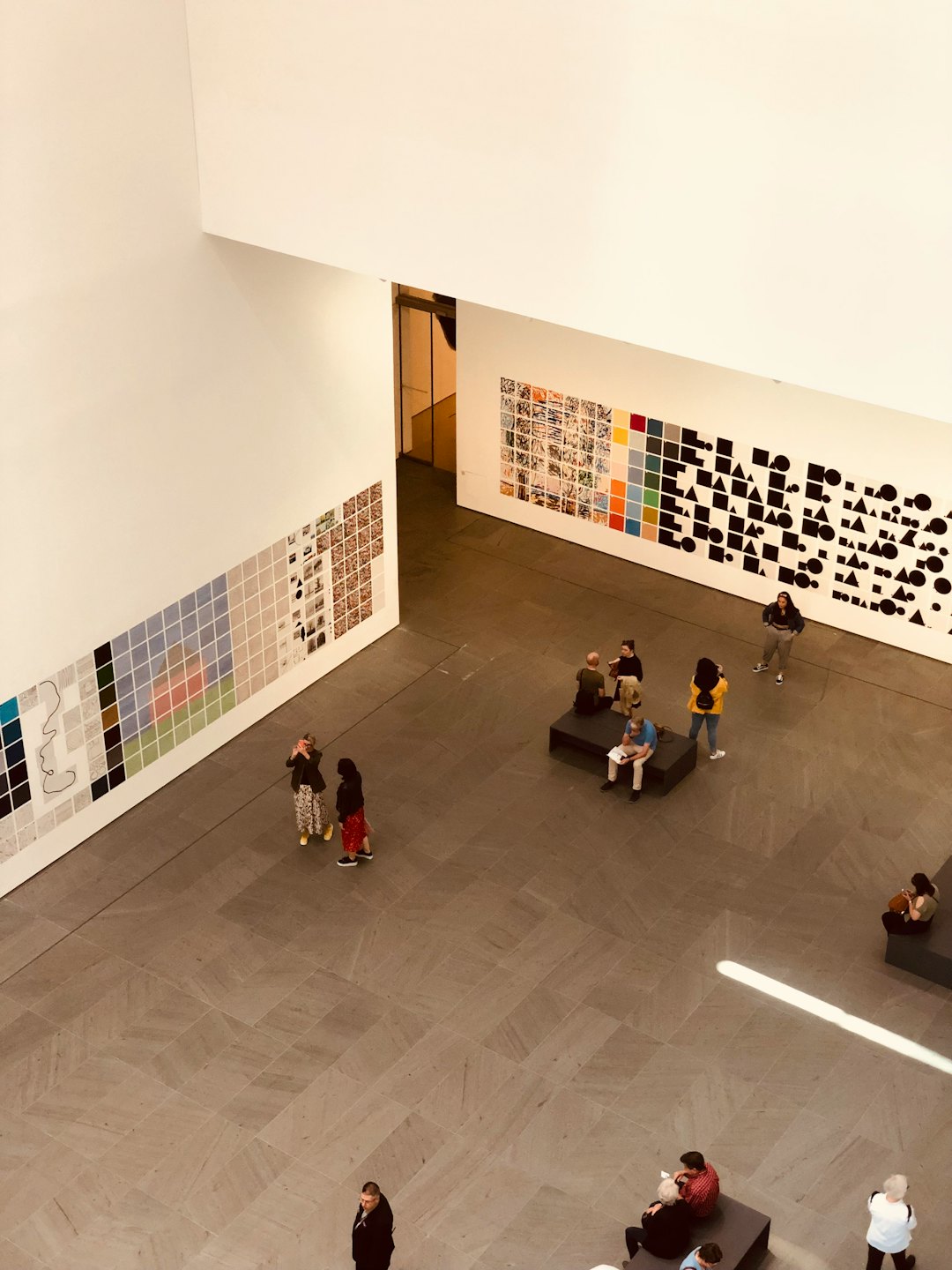 Visitantes pasean y se sientan mientras observan arte en una galería.